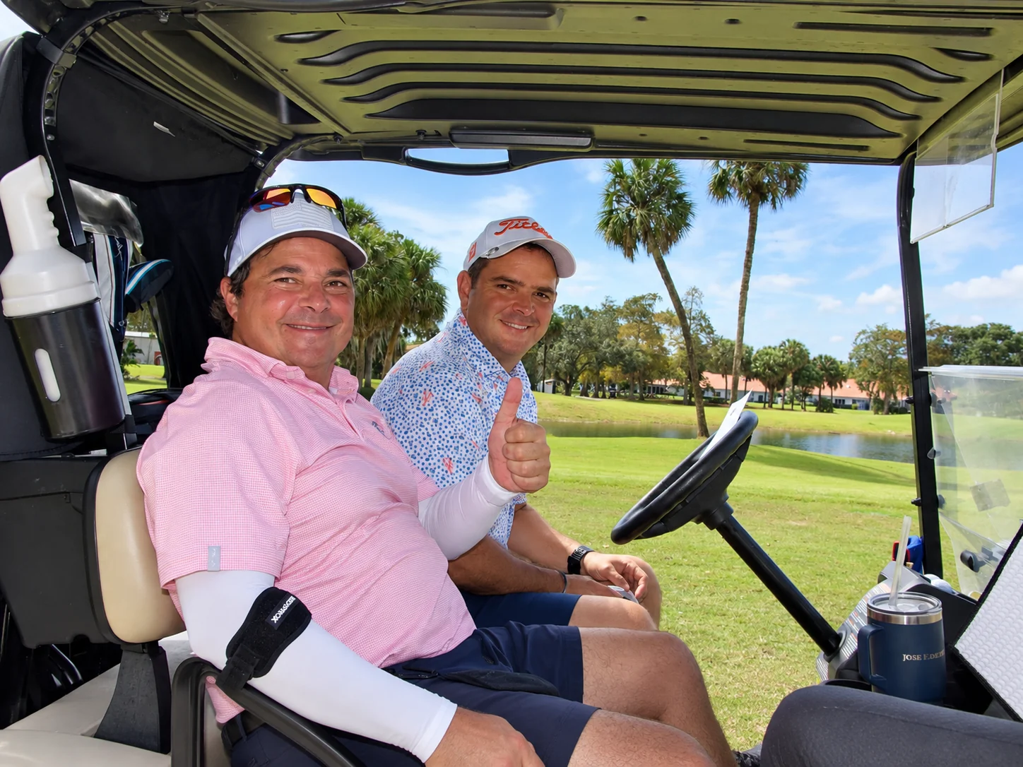 Two players giving a thumbs up from their cart by the lake