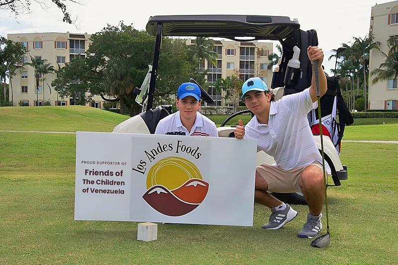 Two players at the Los Andes Foods tee sign supporting Friends of The Children of Venezuela