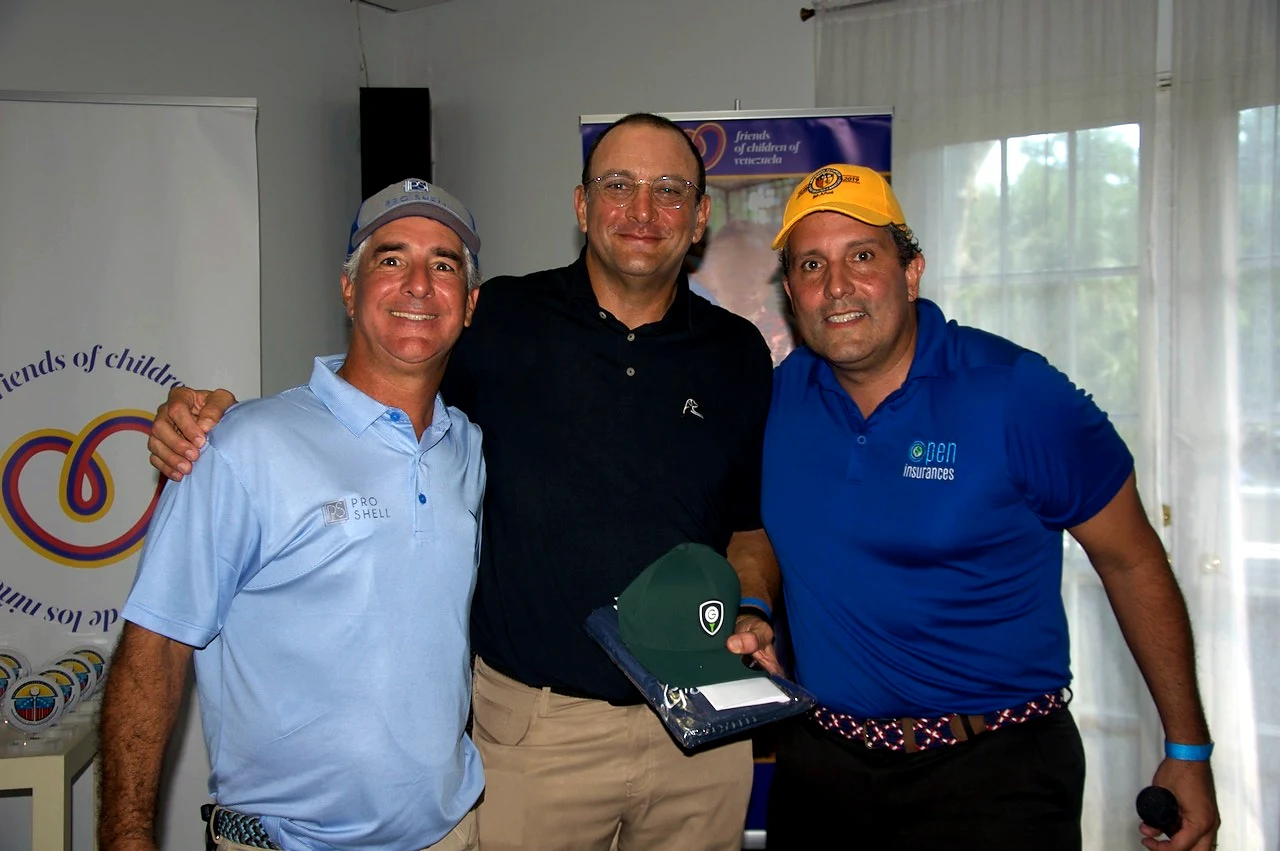 Three supporters with a cap prize in front of the Friends of Children of Venezuela banner