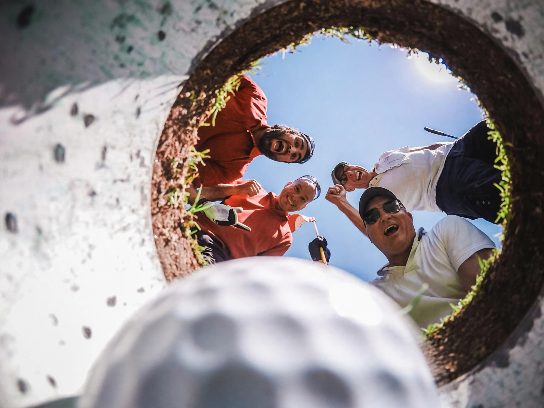 Four friends celebrating together, looking down into the hole with the golf ball in the foreground
