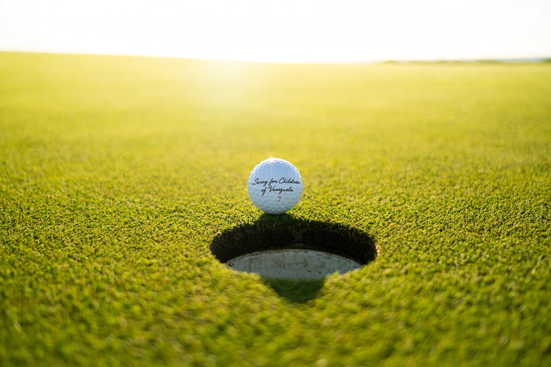 A Swing for Children of Venezuela golf ball on the lip of the cup at sunrise